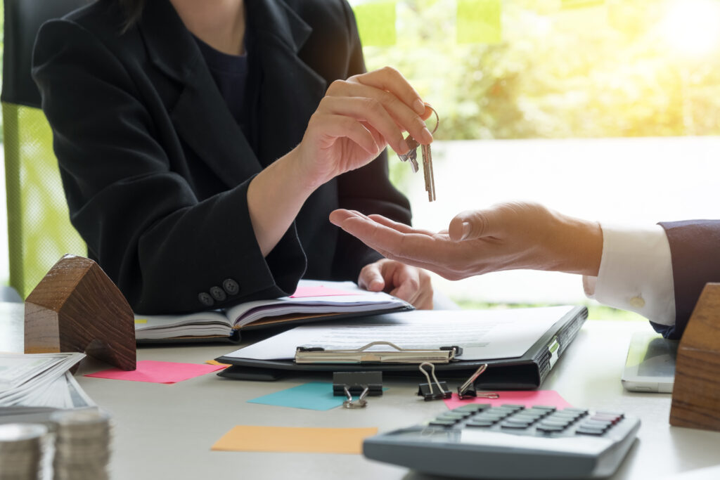 estate agent giving house keys to man and sign agreement with house model, calculator agreement in office